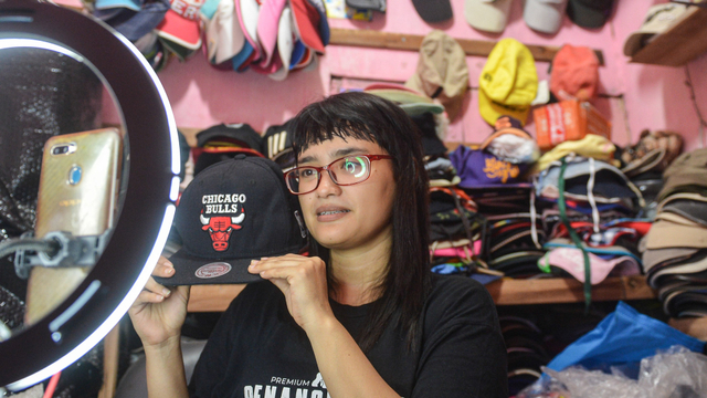 Seorang pedagang menawarkan topi jualannya secara daring melalui jejaring sosial Facebook secara siaran langsung di Jakarta, Minggu (8/8/2021). Foto: M Risyal Hidayat/ANTARA FOTO