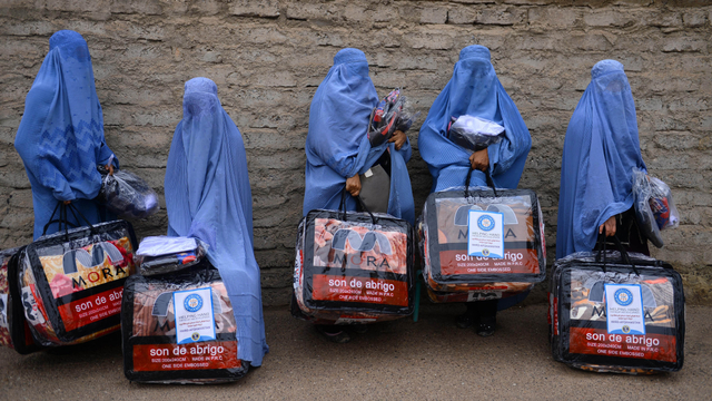 Wanita Afghanistan berpakaian burqa berdiri dengan barang-barang bantuan yang diterima dari sebuah badan amal di Herat. Foto: AFP