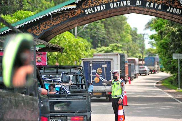 Petugas kepolisian mengarahkan pengemudi untuk berbelok menuju pos penyekatan di pintu masuk Kota Jambi, Jalan Lintas Sumatera, Kota Baru, Jambi, Senin (23/8/2021). Foto: Wahdi Septiawan/Antara Foto