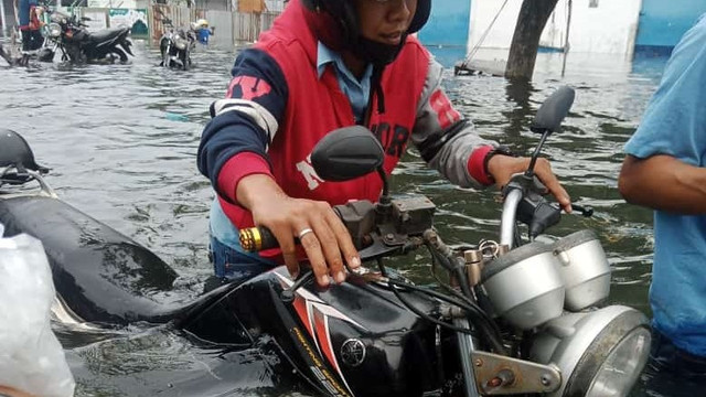 Seorang warga mendorong motor di tengah bencana air rob. Foto: istimewa