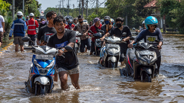 Sejumlah pekerja pelabuhan mendorong motor mereka yang mogok saat menerobos banjir limpasan air laut ke daratan atau rob yang merendam kawasan Pelabuhan Tanjung Emas, Semarang, Jawa Tengah, Selasa (24/5/2022). Foto: Aji Styawan/ANTARA FOTO