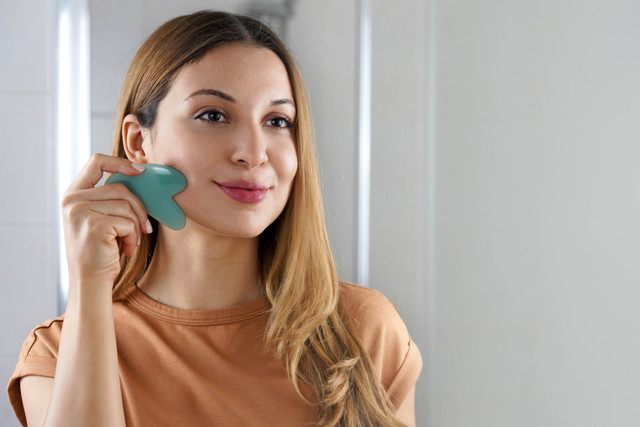 Ilustrasi perempuan memijat wajah dengan Gua Sha. Foto: Shutterstock