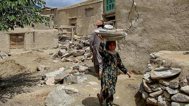 Seorang anak membawa peralatan di kepalanya berjalan melewati rumah-rumah yang rusak setelah gempa bumi di distrik Gayan, provinsi Paktika, Afghanistan, Rabu (22/6/2022). Foto: AFP