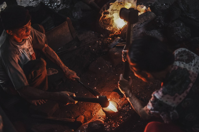 Puang Baddu (75) bersama istrinya bergantian menempa besi yang telah dipanaskan dalam bilik kecil miliknya di Desa Barania, Sinjai Barat, Sulawesi Selatan. Foto: Jumadil Awal