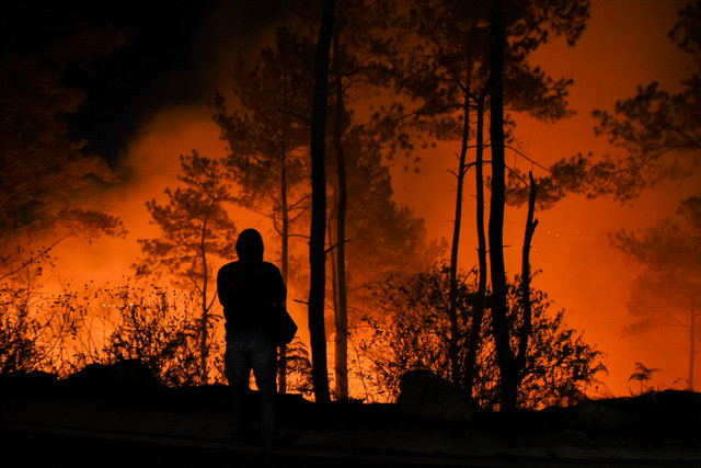 Warga berdiri di dekat lahan yang terbakar di Desa Simulop, Pangururan, Samosir, Sumatera Utara, Minggu (7/8/2022) malam. Foto: Fransisco Carolio/Antara Foto