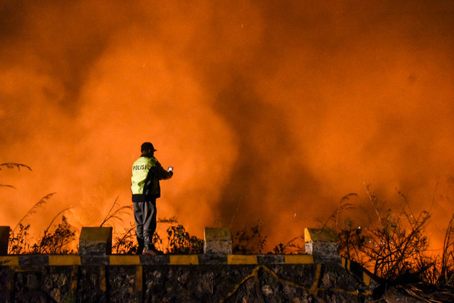 Petugas kepolisian merekam gambar di lokasi kebakaran lahan, Bukit Parombahan, Desa Aek Sipitudai, Sianjur Mulamula, Samosir, Sumatera Utara, Minggu (7/8/2022) malam. Foto: Fransisco Carolio/Antara Foto