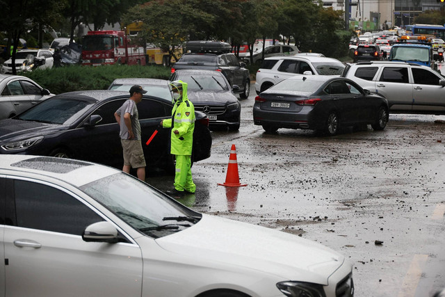 Seorang pria berbicara dengan seorang polisi di sebelah kendaraannya yang terendam banjir di jalanan saat hujan deras pada malam sebelumnya, di Seoul, Korea Selatan, Selasa (9/8/2022). Foto: Kim Hong-Ji/REUTERS
