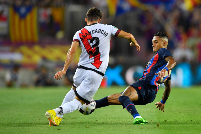Bek Spanyol Rayo Vallecano Fran Garcia (kiri) ditekel oleh pemain depan Barcelona asal Brasil Raphinha selama pertandingan sepak bola liga Spanyol antara FC Barcelona dan Rayo Vallecano de Madrid di stadion Camp Nou di Barcelona pada 13 Agustus 2022. Foto: PAU BARRENA/AFP