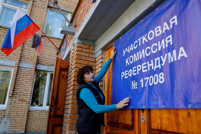 Seorang anggota komisi pemilihan lokal memasang spanduk di pintu-pintu tempat pemungutan suara menjelang rencana referendum tentang bergabungnya Republik Rakyat Donetsk ke Rusia, di Donetsk, Ukraina. Foto: Alexander Ermochenko/REUTERS