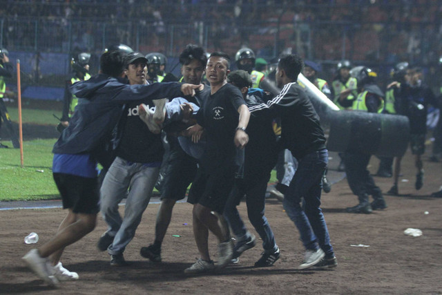 Penonton membawa rekannya yang pingsan akibat sesak nafas terkena gas air mata yang ditembakkan aparat keamanan saat kericuhan usai pertandingan sepak bola BRI Liga 1 antara Arema melawan Persebaya di Stadion Kanjuruhan, Malang, Sabtu (1/10). Foto: Ari Bowo Sucipto/ANTARA FOTO