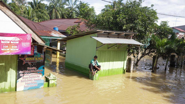 Warga duduk di atas tembok kiosnya di tengah suasana banjir yang melanda Kabupaten Aceh Tamiang. Foto: Suparta/acehkini 