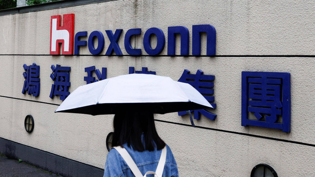 Seorang wanita membawa payung berjalan melewati logo Foxconn di luar gedung perusahaan di Taipei, Taiwan Senin (31/10/2022). Foto: Carlos Garcia Rawlins
