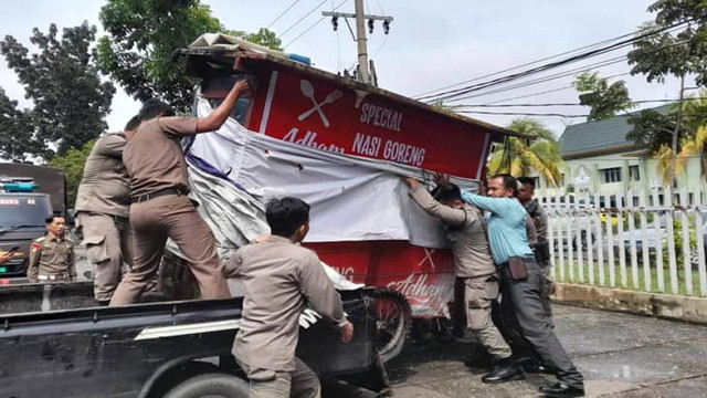 Petugas Satpol PP Kota Pekanbaru mengangkut lapak dan gerobak yang ditinggal PKL saat penertiban. (LARAS OLIVIA/SELASAR RIAU)