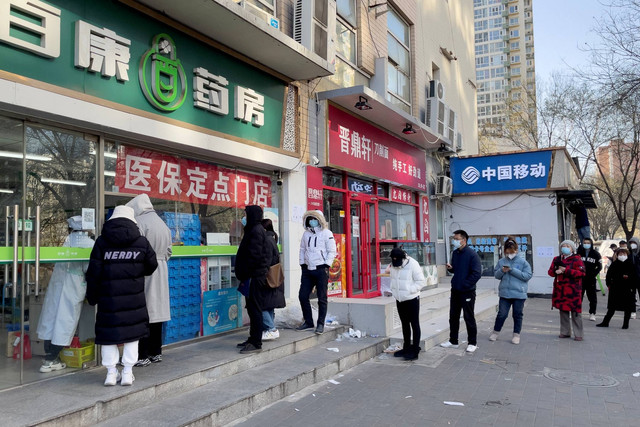 Orang-orang yang memakai masker mengantre di luar apotek untuk membeli obat di sebuah apotek di Beijing, China, Selasa (6/12/2022). Foto: Alessandro Diviggiano/REUTERS