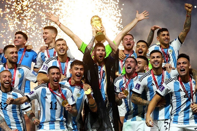 Pemain Argentina Lionel Messi berselebrasi dengan trofi bersama rekan setimnya setelah memenangkan Piala Dunia 2022, di Stadion Lusail, Lusail, Qatar, Minggu (18/12/2022). Foto: Kai Pfaffenbach/REUTERS