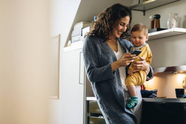 seorang anak yang dikasih liat handphone oleh sang ibu agar tidak menangis, https://www.istockphoto.com/id/foto/wanita-tersenyum-dengan-sms-bayi-di-telepon-di-rumah-gm1314404449-402636070
