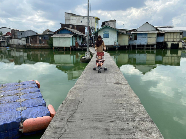 Warga sedang melintasi jembatan panjang tanpa pembatas yang berada di Kampung Apung, Kapuk Teko, Kapuk, Cengkareng, Jakarta Barat, Senin (19/12/22). Foto: Nabilatul Dzakiyyah/Kumparan