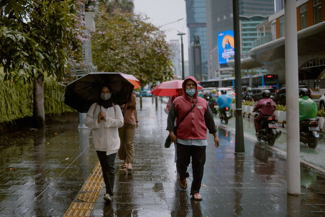 Sejumlah warga berjalan di dekat anjungan halte Bundaran Hotel Indonesia saat hujan ringan, Jakarta, Rabu (28/12/2022). Foto: Jamal Ramadhan/kumparan