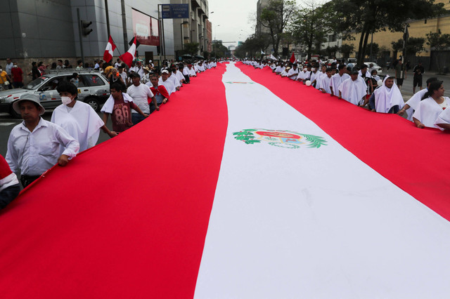 Demonstran memegang bendera nasional raksasa saat mereka berpartisipasi dalam pawai meminta perdamaian, setelah protes kekerasan saat penggulingan dan penangkapan mantan Presiden Pedro Castillo di Lima, Peru, Selasa (3/1/2023). Foto: Sebastian Castaneda/REUTERS