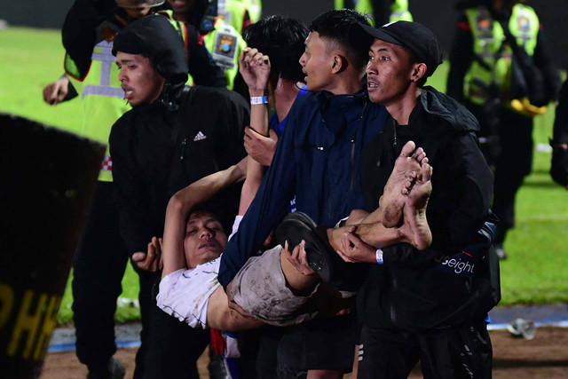 Sekelompok orang menggendong seorang pria usai pertandingan sepak bola antara Arema FC dan Persebaya Surabaya di stadion Kanjuruhan, Malang, Jawa Timur (1/10/2022) Foto: STR/AFP