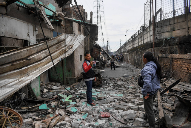 Warga berfoto tak jauh dari permukiman yang hangus terbakar dan hancur pascakebakaran Depo Pertamina Plumpang di Jalan Koramil, Rawa Badak Selatan, Koja, Jakarta, Sabtu (4/3/2023). Foto: M Risyal Hidayat/ANTARA FOTO