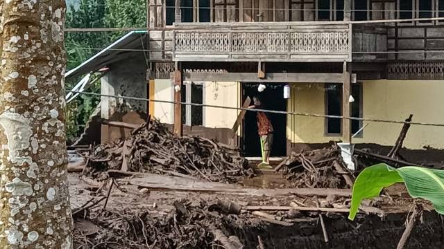 Seorang warga di Desa Klabat, Kabupaten Minahasa Utara membersihkan rumahnya dari sisa sampah banjir bandang
