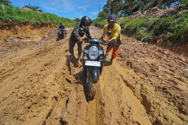 Kubangan Lumpur - Warga mendorong sepeda motornya melewati jalan rusak di Desa Persiapan Air Merah, Muaro Jambi, Jambi, Selasa (9/5/2023). Foto: Wahdi Septiawan/Antara Foto