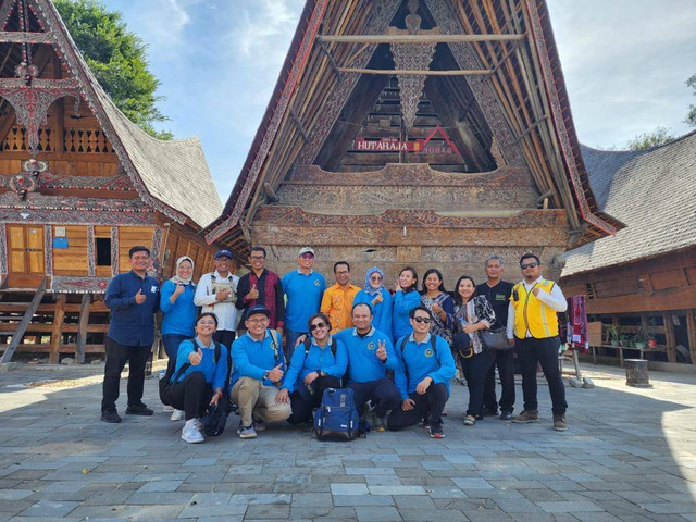 Penulis dan rombongan berfoto di depan salah satu rumah adat di Kampung Ulos Huta Raja. (Foto: Dokumentasi Pribadi)