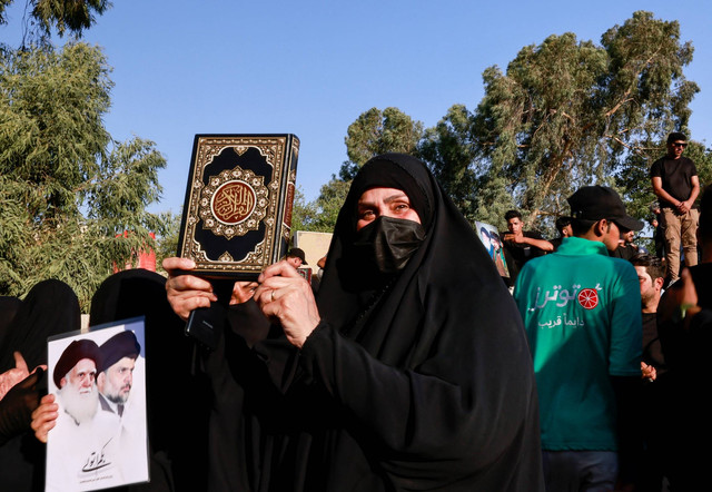 Seorang wanita memegang mushaf Al-Qur'an saat protes terhadap seorang pria yang merobek dan membakar mushaf Al-Qur'an di luar masjid di ibu kota Swedia, Stockholm, dekat kedutaan Swedia di Baghdad, Irak, Jumat (30/6/2023). Foto: Thaier Al-Sudani/REUTERS