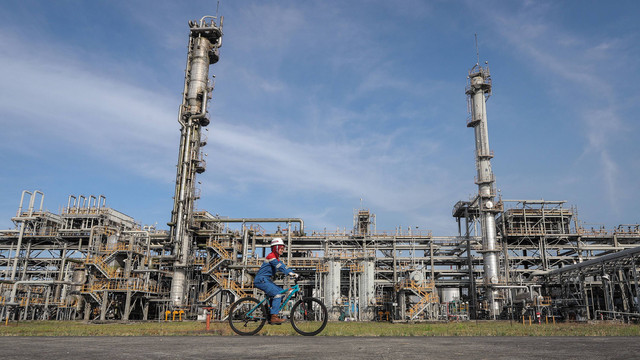 Pekerja bersepeda dengan latar belakang LPG Facility di kawasan Onshore Processing Facility (OPF) Saka Indonesia Pangkah Limited (SIPL), Gresik, Jawa Timur, Kamis (13/7/2023). Foto: ANTARA FOTO/Rizal Hanafi
