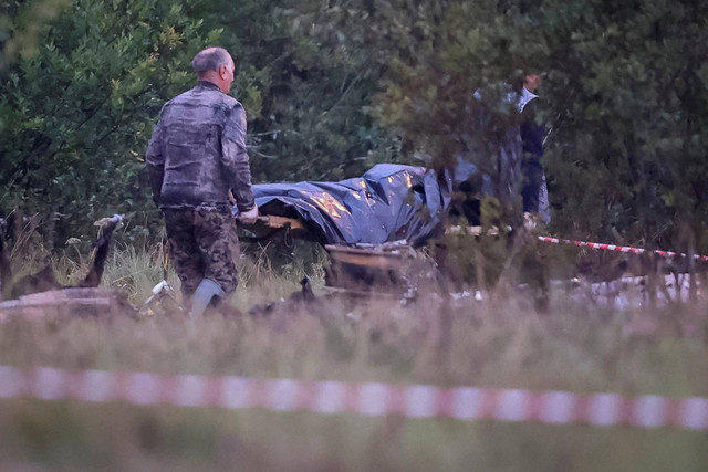 Spesialis darurat membawa kantong mayat di dekat puing-puing jet pribadi yang terkait dengan kepala tentara bayaran Wagner Yevgeny Prigozhin di dekat lokasi kecelakaan di wilayah Tver, Rusia, Kamis (24/8/2023). Foto: Anton Vaganov/REUTERS
