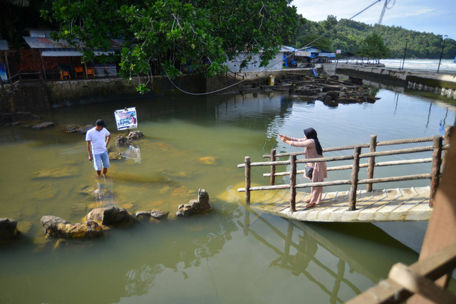 Pengunjung berdiri di area batu Malin Kundang yang terendam banjir, di Pantai Air Manis, Padang, Sumatera Barat, Senin (28/8/2023). Foto: Iggoy el Fitra/ANTARA FOTO