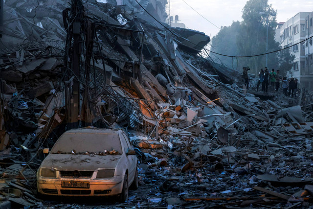 Sebuah mobil rusak di tengah reruntuhan menara yang hancur akibat serangan udara Israel di Kota Gaza, Sabtu (7/10/2023).  Foto: Mohammed ABED / AFP