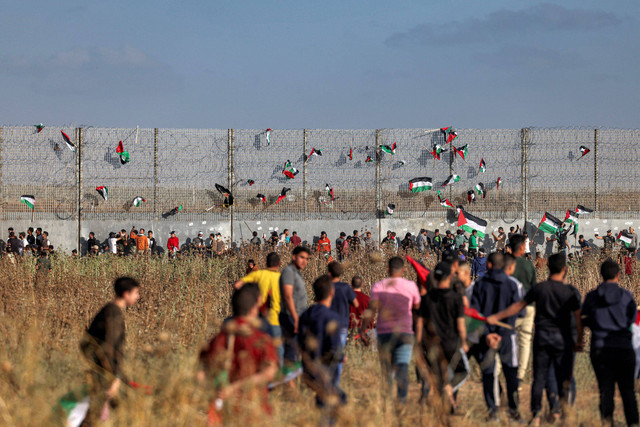 Bendera Palestina dipasang di pagar kawat berduri saat demonstrasi 'pawai bendera' di sepanjang perbatasan dengan Israel di sebelah timur kota Gaza pada 18 Mei 2023. Foto: Mohammed Abed/AFP
