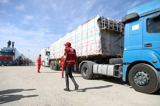 Anggota dan sukarelawan Bulan Sabit Merah Mesir berkumpul di samping truk yang membawa bantuan kemanusiaan dari LSM Mesir yang melewati penyeberangan Rafah dari sisi Mesir, di Rafah, Mesir, Sabtu (21/10/2023). Foto: Stringer/REUTERS