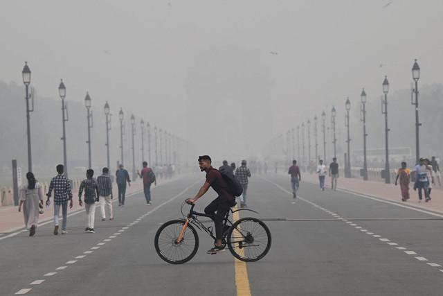 Orang-orang berjalan di sepanjang Jalur Kartavya dekat Gerbang India di tengah kondisi kabut asap tebal di New Delhi, India, Jumat (3/11/2023). Foto: Arun Thakur/AFP