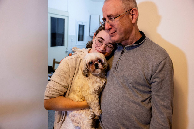 Mia Leimberg (17), menggendong anjingnya, Bella, sambil menyandarkan kepalanya di bahu ayahnya, Moshe, sepekan setelah dibebaskan Hamas.  Foto: REUTERS/Ronen Zvulun