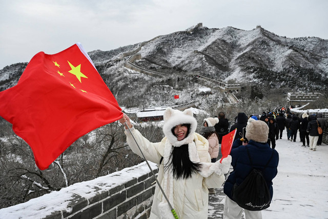 Seorang wanita berpose dengan bendera nasional China di Tembok Besar China di Badaling, utara Beijing, setelah hujan salju semalaman, Jumat (15/12/2023). Foto: Greg Baker/AFP