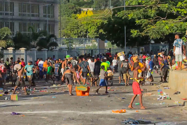 Warga berlarian membawa membawa barang-barang rampasan di tengah kerusuhan di Port Moresby, Papua Nugini, Rabu (10/1/2024). Foto: STR/AFP
