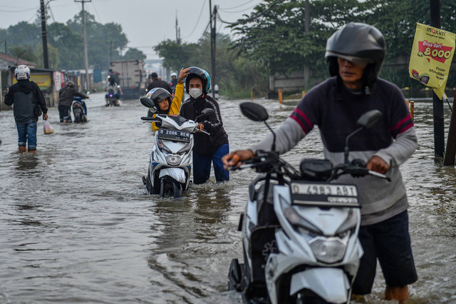 Warga mendorong motornya yang mogok saat melintasi banjir di Kawasan Industri Sapan, Kabupaten Bandung, Jawa Barat, Jumat (12/1/2024). Foto: ANTARA FOTO/Raisan Al Farisi