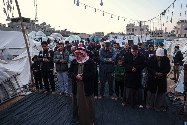 Warga Palestina berdoa sebelum berbuka puasa pada hari pertama bulan suci Ramadhan, di sebuah kamp pengungsi di Rafah di Jalur Gaza selatan pada 11 Maret 2024, di tengah pertempuran yang sedang berlangsung antara Israel dan kelompok militan Hamas. Foto: Kata Khatib/AFP