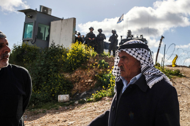 Tentara Israel berjaga ketika warga Palestina tiba di pos pemeriksaan di Qalandia, di Tepi Barat, untuk salat Jumat pertama bulan Ramadan di masjid Al Aqsa, Jumat (15/3/2024). Foto: Jaafar Ashtiyeh/AFP