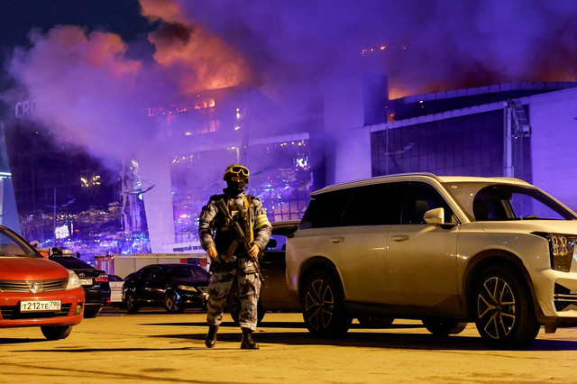 Seorang petugas penegak hukum Rusia berjalan di area parkir dekat tempat konser Balai Kota Crocus yang terbakar setelah insiden penembakan, di luar Moskow, Rusia, Jumat (22/3/2024). Foto: Maxim Shemetov/REUTERS