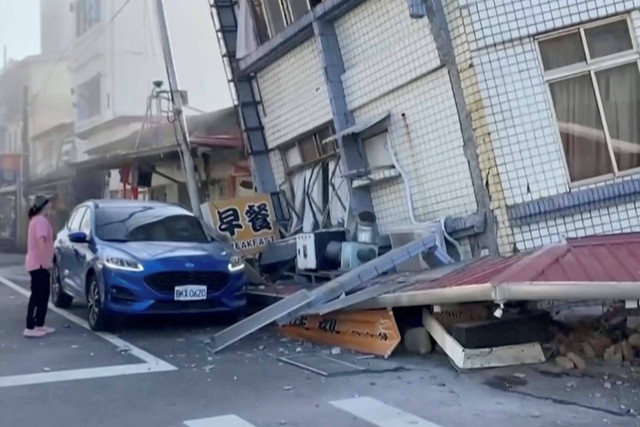 Dalam gambar yang diambil dari rekaman video yang ditayangkan TVBS, seorang wanita berdiri di dekat bangunan yang sebagian runtuh di Hualien, Taiwan timur pada Rabu, (3/4/2024) Foto: TVBS/AP