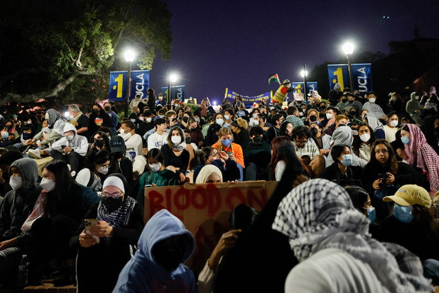 Pengunjuk rasa pro-Palestina duduk di tangga menuju perkemahan yang didirikan oleh mahasiswa dan aktivis pro-Palestina saat mereka berdemonstrasi di kampus Universitas California, Los Angeles (UCLA) di Los Angeles, California (1/5/2024). Foto: ETIENNE LAURENT / AFP