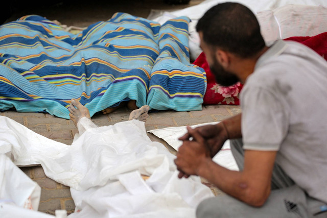 Seorang pria Palestina duduk di dekat mayat orang-orang yang tewas dalam pemboman Israel, di halaman Rumah Sakit Martir Al-Aqsa di Deir al-Balah di Jalur Gaza tengah pada Sabtu (11/5/2024). Foto: AFP