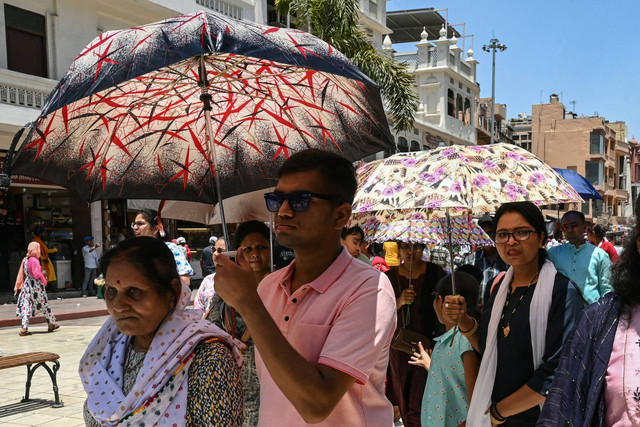 Wisatawan berjalan dengan payung untuk melindungi diri dari sinar matahari, pada hari musim panas saat gelombang panas di Amritsar (10/6/2024). Foto: NARINDER NANU / AFP