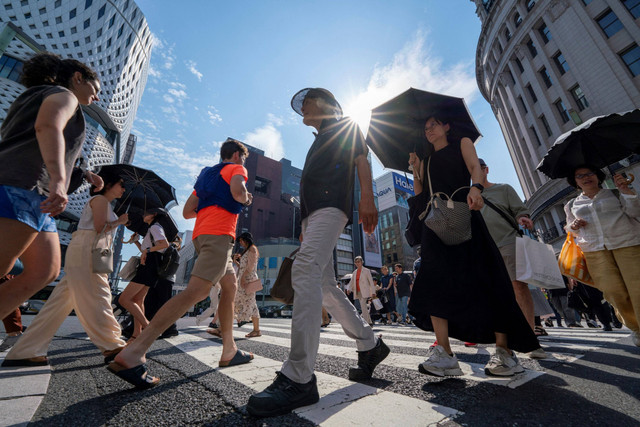 Sejumlah pejalan kaki memakai payung saat suhu panas mencapai 35 derajat celcius di pusat kota Tokyo, Jepang, Senin (8/7/2024). Foto: Kazuhiro NOGI / AFP