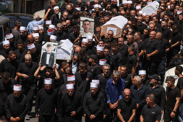 Para tetua Druze dan pelayat mengelilingi peti mati 10 dari 12 orang yang terbunuh dalam serangan roket. (28/7/2024). Foto: MENAHEM KAHANA / AFP