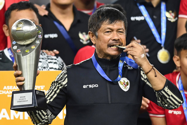 Pelatih Timnas Indonesia Indra Sjafri menggigit medali dan mengangkat Piala AFF U-19 di Stadion Gelora Bung Tomo, Surabaya, Jawa Timur, Senin (29/7/2024). Foto: Sigid Kurniawan/ANTARA FOTO